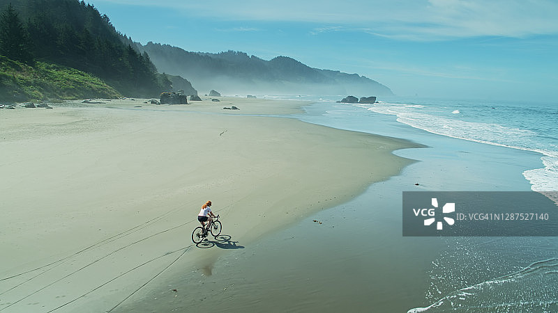 红头发的女人在鲸鱼头海滩上骑自行车-天线图片素材