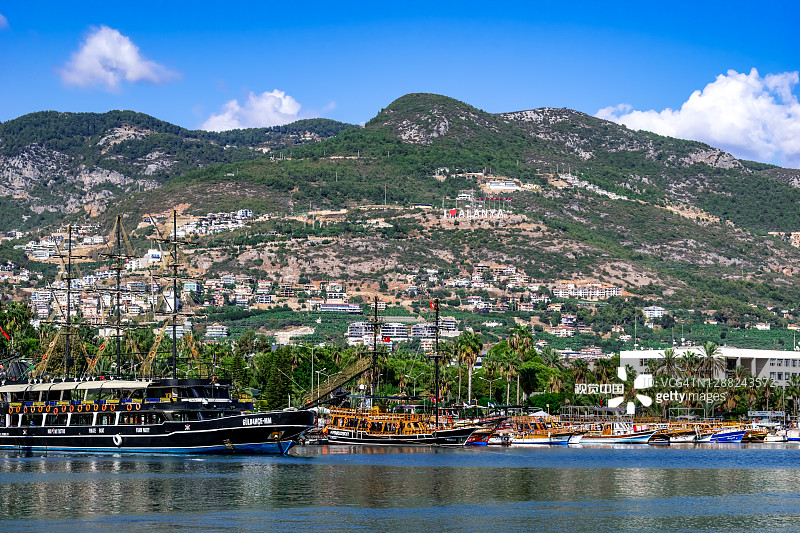 土耳其小镇的海岸线，山上写着“我爱阿兰亚”。美丽的风景与船舶和游艇的背景与热带异国城市的棕榈树图片素材