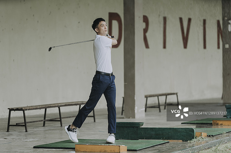 成熟的亚洲华人男子在练习场挥动他的高尔夫球杆图片素材