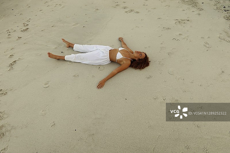 一个穿着白色裤子和比基尼上衣的女人在海滩上伸开双臂图片素材