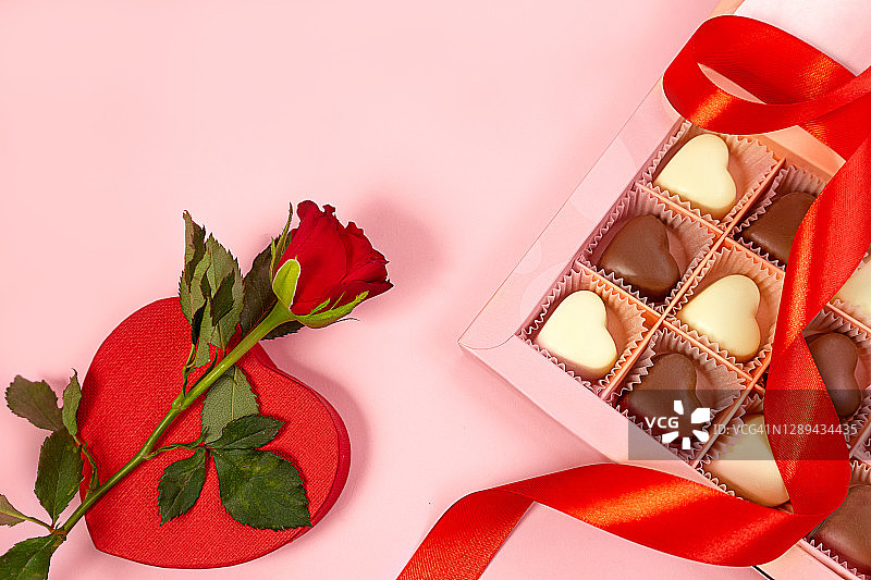 粉色背景下的情人节红玫瑰、心形盒子和巧克力糖果。图片素材