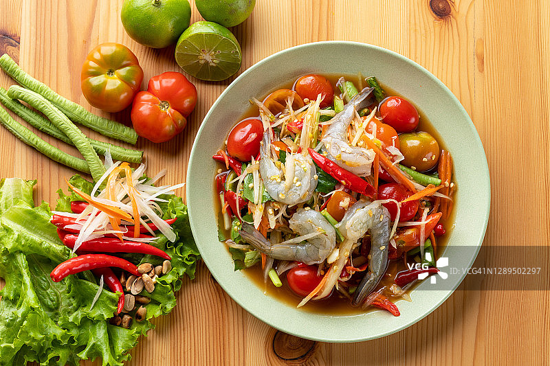 俯视图绿色木瓜沙拉与鲜虾和菜单成分在绿色盘子上木制背景，泰国食物图片素材