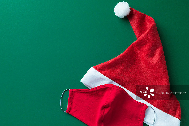 红色医用防护口罩、无檐小便帽或圣诞老人帽，以绿色为背景。预防和预防COVID - 19大流行的传播。快乐健康圣诞的理念。图片素材