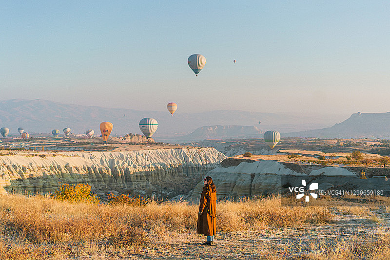 在土耳其卡帕多西亚，一名妇女站在那里观看热气球图片素材