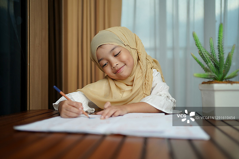一个穆斯林孩子一边做作业一边看书。孩子喜欢在家里快乐地学习。聪明，教育和聪明的学习理念。图片素材