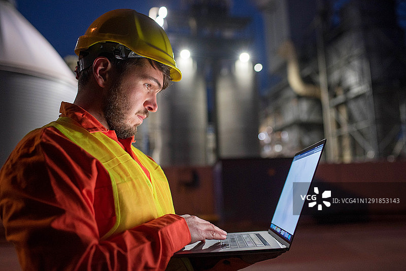 一个年轻的工程师在一个石油工厂前拿着笔记本电脑图片素材
