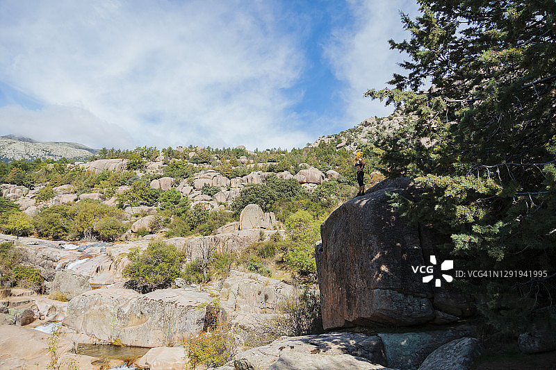 西班牙马德里，一名女徒步者站在森林里的一块巨石上欣赏风景图片素材