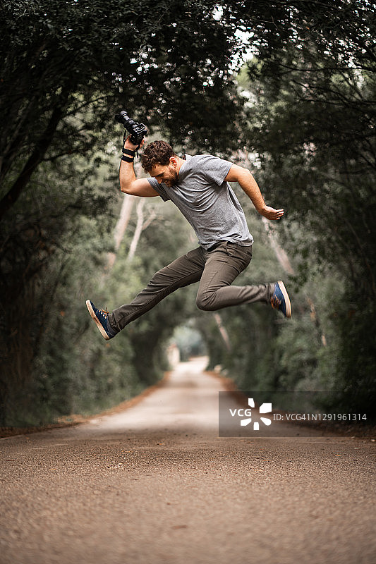 年轻的摄影师跳上一条道路，那里的树木形成了一个隧道图片素材