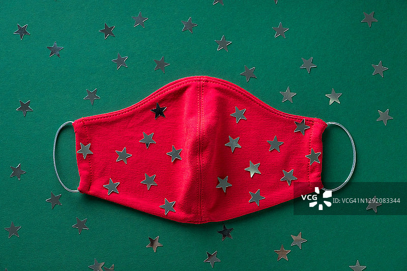 红色医用防护口罩和五彩纸屑在绿色圣诞背景上。预防和预防COVID - 19大流行的传播。预防病毒、感染和肺炎。一个快乐健康的圣诞理念。图片素材