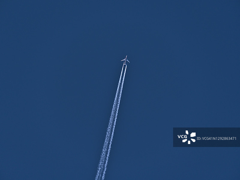 低角度的高飞行双引擎飞机与凝结尾迹在晴朗的蓝天。图片素材