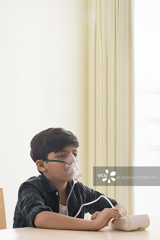 小男孩坐在家里通过喷雾器吸入空气。(儿童)图片素材