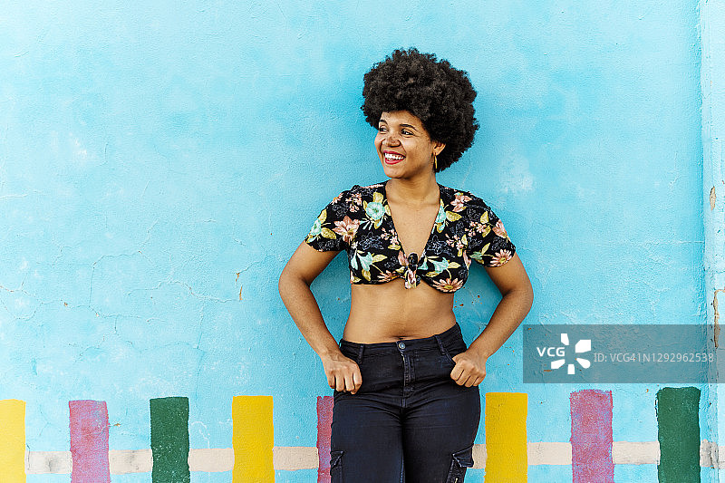 一位非裔美国妇女面带微笑，站在一堵蓝色的墙前，向一边看图片素材