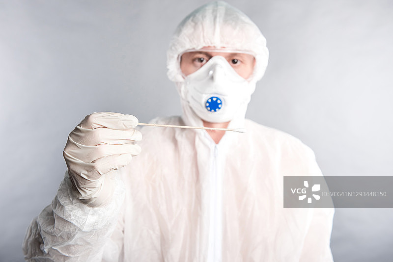 身穿防护服的医生手持棉签进行COVID-19冠状病毒检测涂片图片素材