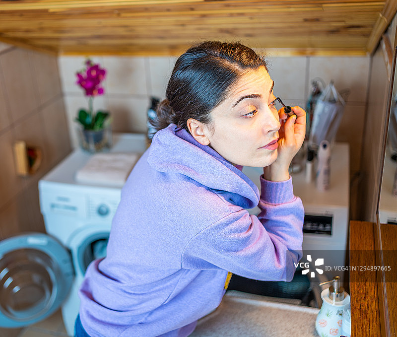 一个年轻女子在家里的浴室里涂睫毛膏。图片素材