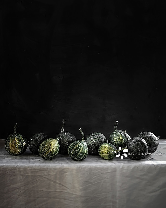 食物摄影组绿色迷你南瓜正面视图在白色桌布上的黑色粉笔板墙背景近图片素材