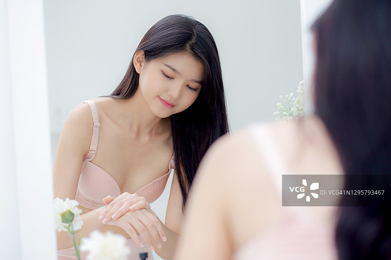 美丽性感的年轻亚洲女人照镜子，在手上涂抹霜和信息，美丽的女孩应用身体乳液护肤健康和柔软的水，治疗和化妆品与保湿。图片素材