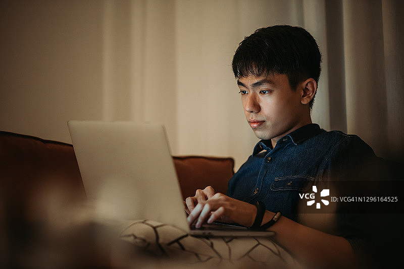 年轻的亚洲华人男性在沙发上使用笔记本电脑在家工作图片素材