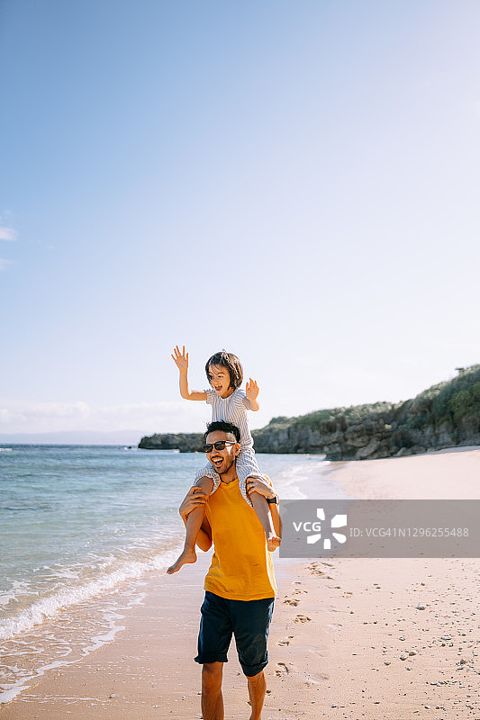 父亲肩上扛着激动的小女儿在热带海滩上图片素材