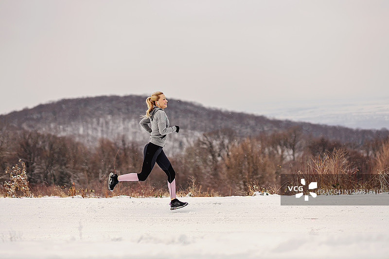 女运动员在冬天的雪道上奔跑。健康的生活方式，冬天健身，寒冷的天气图片素材