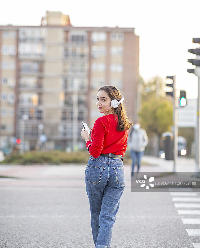 一个女人站在城市的街道上戴着耳机听音乐图片素材
