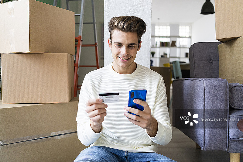 一个微笑的年轻人在搬家时用信用卡支付手机图片素材