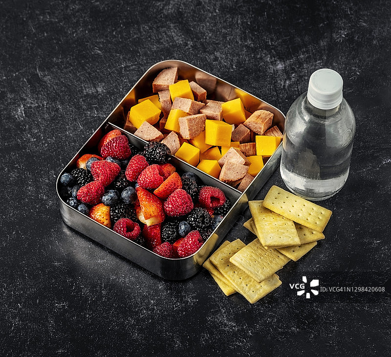 午餐盒(浆果奶酪和意大利腊肠)和一瓶水在黑色的背景图片素材