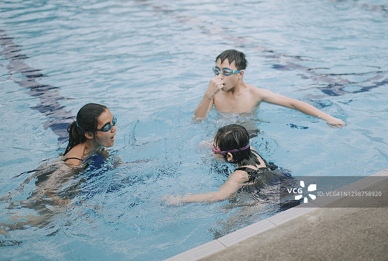 亚洲华人的孩子们在游泳池里跟他们的教练学习游泳图片素材