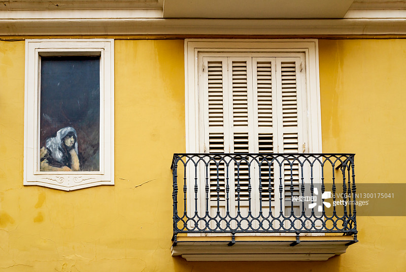 西班牙巴伦西亚历史悠久的西班牙住宅立面，带有阳台和一幅壁画，画中是一位妇女望向窗外，西班牙图片素材