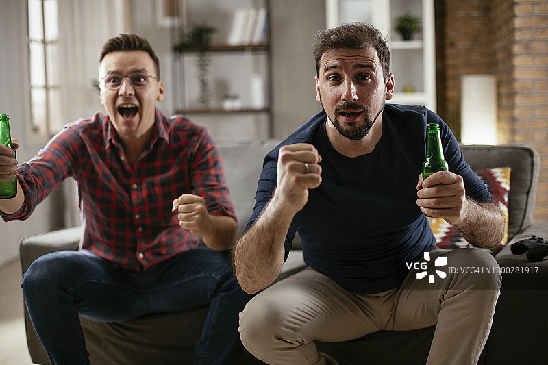 男人喝啤酒，看电视上的体育比赛。图片素材