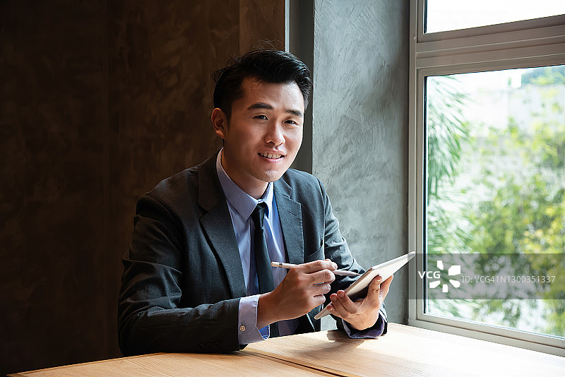 聪明和自信的年轻亚洲企业家企业家在他的工作站使用数字平板电脑的肖像。图片素材