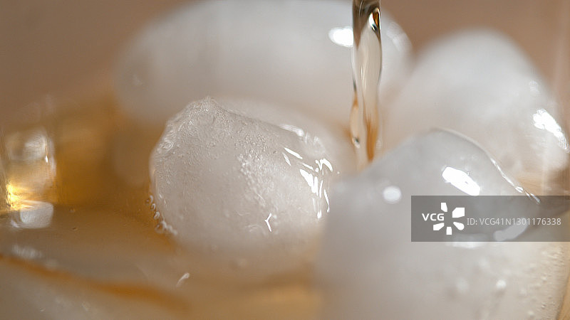 MACRO:将美味的波旁威士忌倒在玻璃杯中闪亮融化的冰上。图片素材