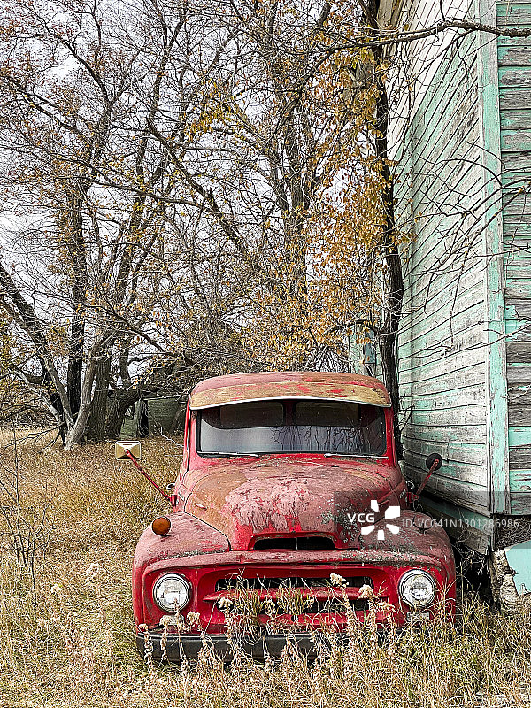 一辆老式红色皮卡停在一间废弃的房子旁边图片素材
