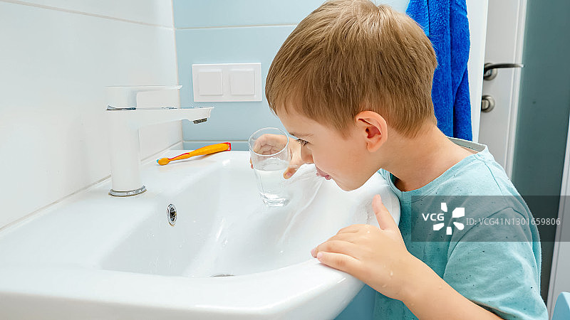 微笑的小男孩在用牙刷和牙膏刷牙后用玻璃杯里的水漱口。牙齿卫生和日常生活的概念图片素材