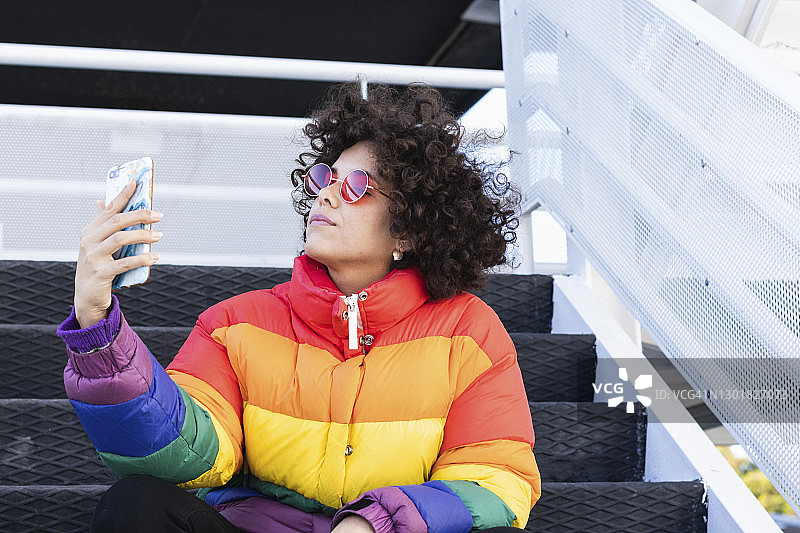 穿着彩色夹克的女子坐在台阶上用手机自拍图片素材