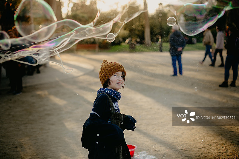 男孩微笑着看着公园里的一个大泡泡图片素材