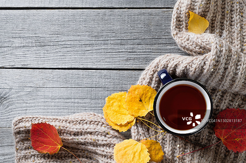 一杯热咖啡或茶，明亮的秋天黄叶，一条温暖舒适的针织羊毛围巾，背景是一个旧的木制背景或桌子。季节性的娱乐、放松和心灵的平静的概念。文本空间的拷贝。图片素材