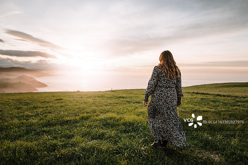 日落时分，年轻女子在绿色的田野上散步图片素材