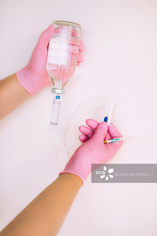 系统与生理盐水在医生的手中在粉红色的手套在白色的背景。新冠肺炎疫情期间的隔离和医疗理念图片素材