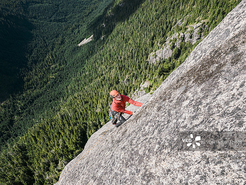 攀岩者攀登一个高高的岩面，高于一个森林覆盖的山谷图片素材