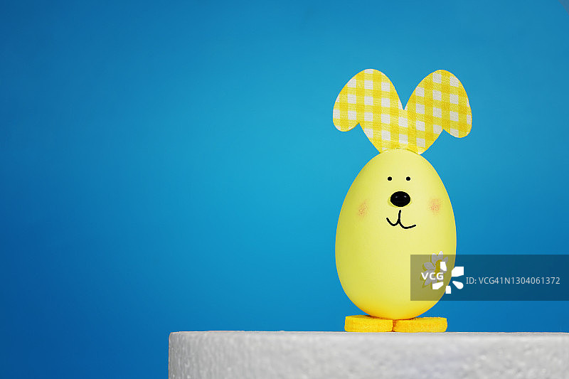 黄色的复活节兔子在蓝色的背景上的一个蛋的形式。复活节背景概念，为文字。图片素材