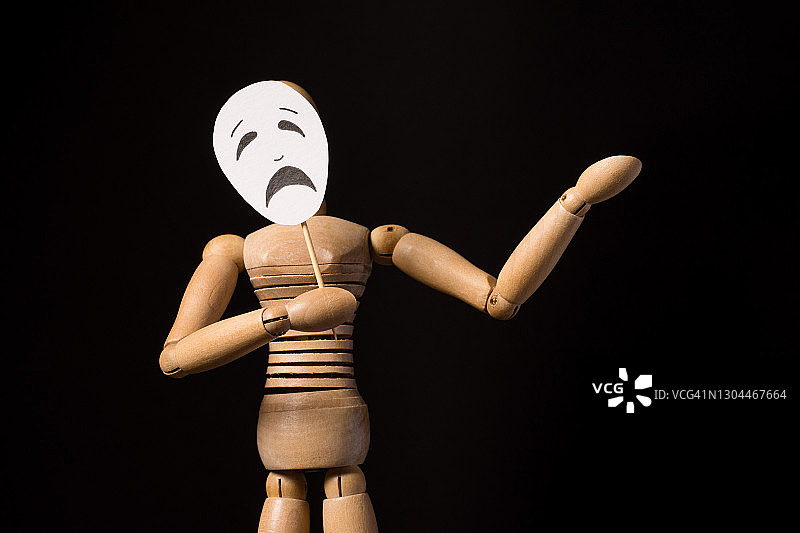 木制木偶玩偶在铰链持有一个面具在手中和覆盖脸在一个黑色的背景图片素材