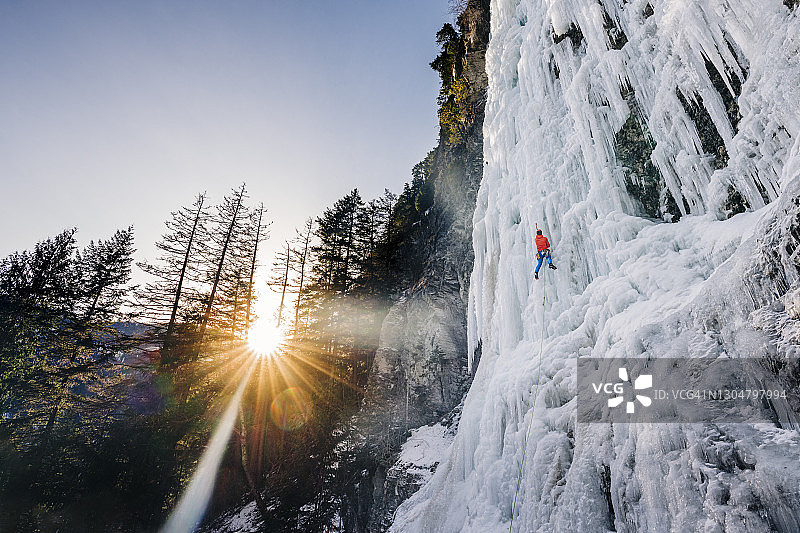 一个冰上攀登者攀登一个高高的冰冻瀑布，就像在一个戏剧性的日出图片素材