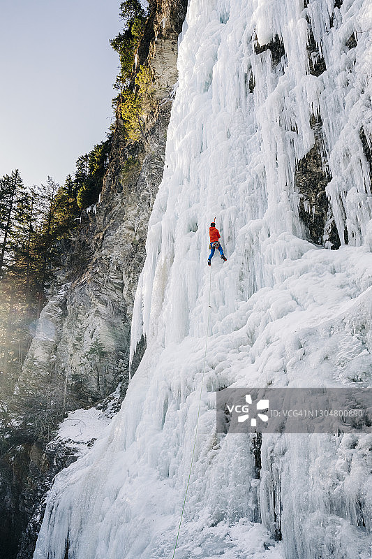 清晨，冰攀登者站在结冰的瀑布上，沐浴着明亮的阳光图片素材