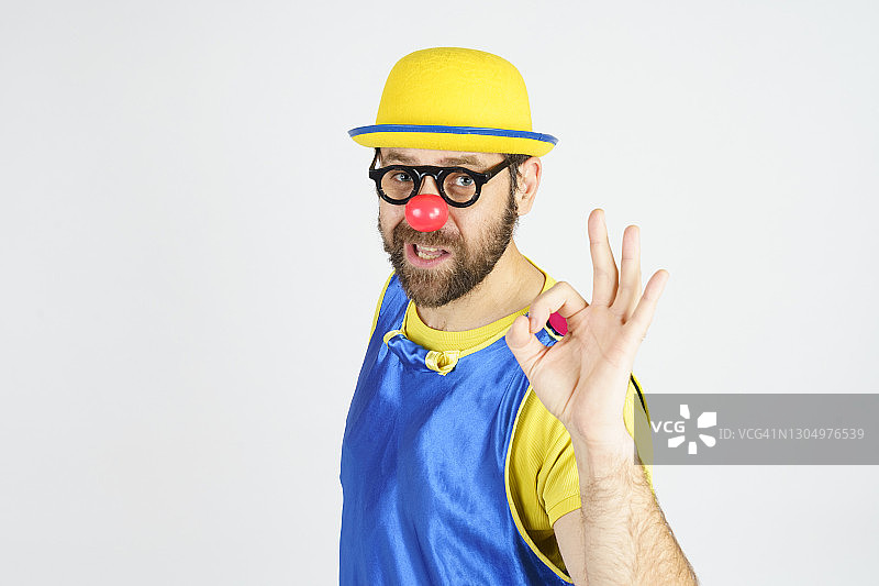 一个小丑穿着亮蓝色和黄色的衣服，戴着眼镜和帽子，显示了一个OK的手势图片素材