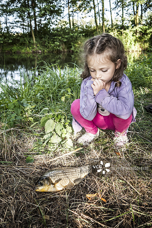 在波兰，一个女孩蹲在河边看着一条刚捕到的鱼图片素材