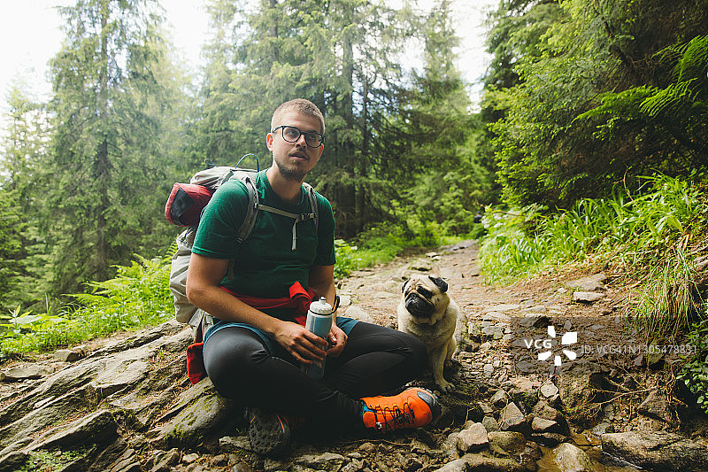 一个背着背包的年轻人和他的狗在森林里徒步旅行图片素材