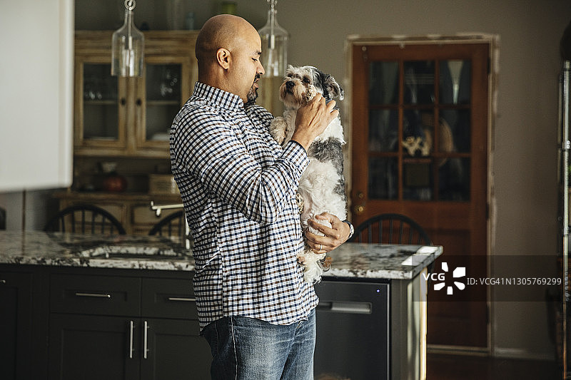 男人抱着狗站在家里的厨房里图片素材