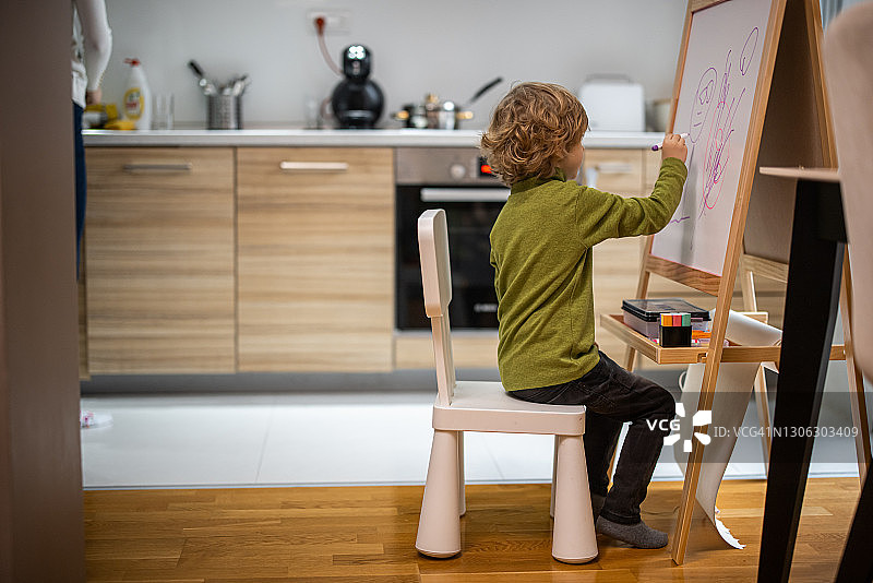 小男孩坐在椅子上，在白色黑板上画画图片素材