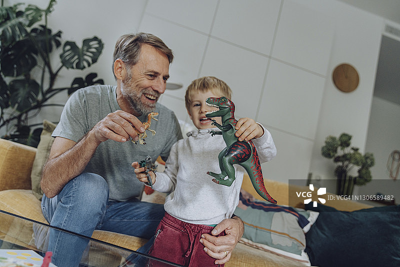 爸爸和儿子在客厅里玩恐龙玩具图片素材