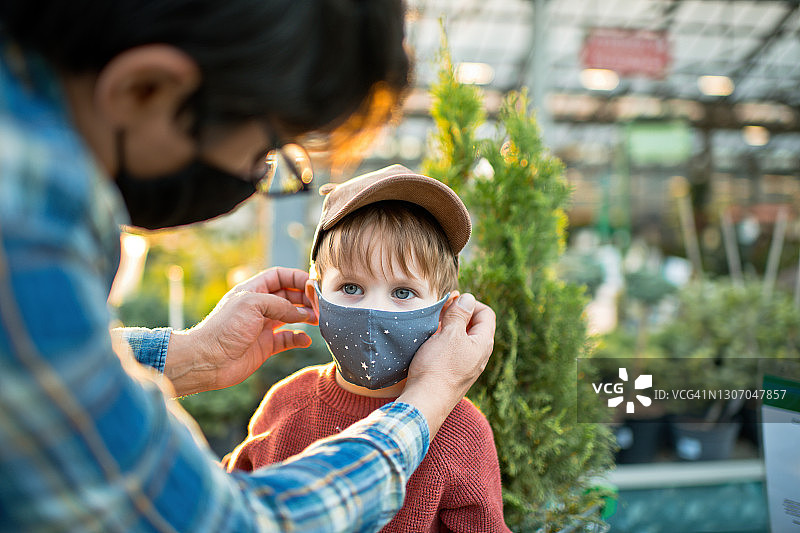 在花园中心购物时，父亲给孩子戴上防护口罩图片素材